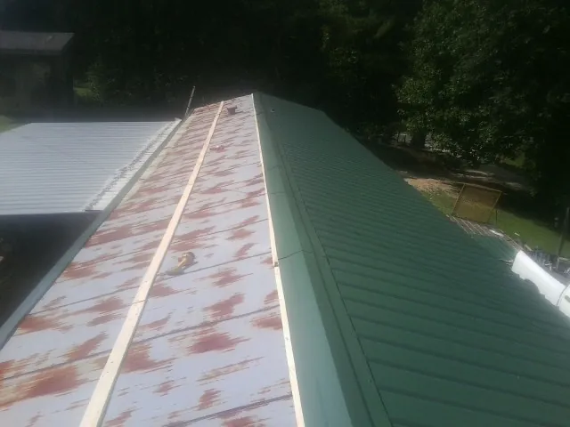 Old rusted panels beside newly installed green metal roofing — Wind Damage Roof Repair by Roofing Brothers in Fox Island
