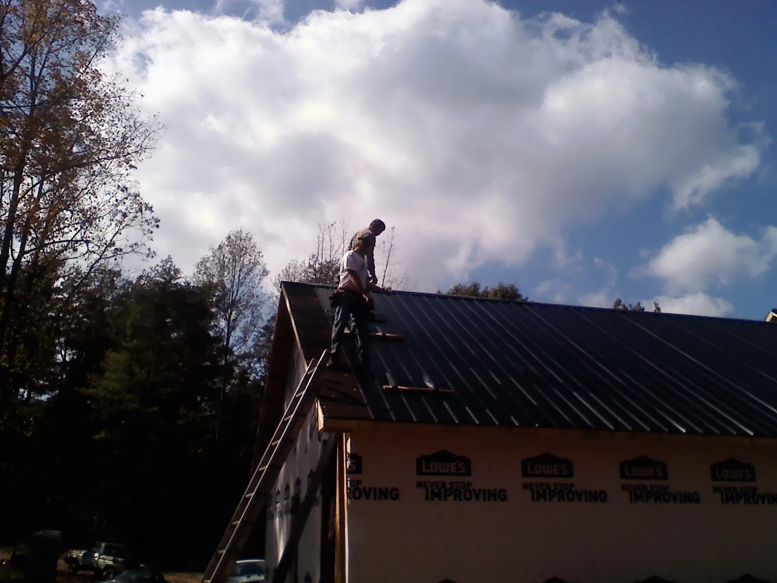 Roofer fastening dark metal panels high against a cloudy sky, from a Roof Inspection job in Fox Island