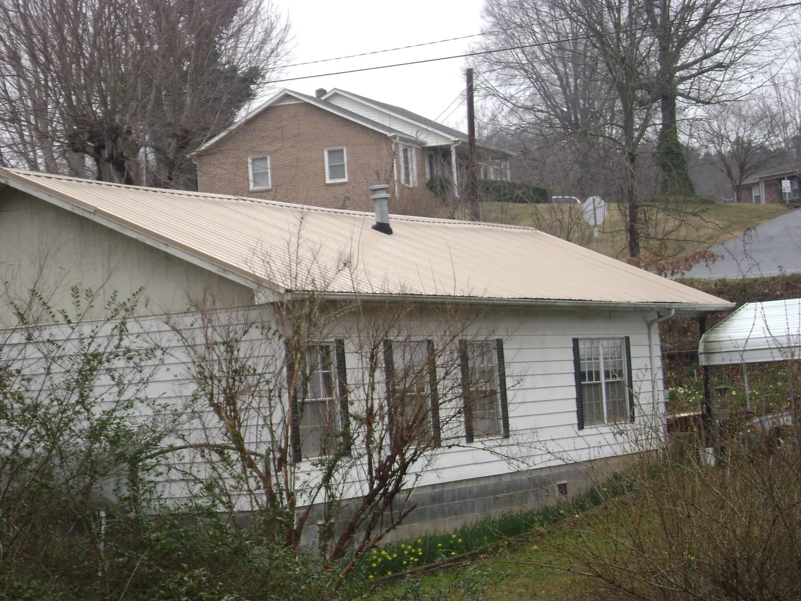 Tan metal roof on a white sided house set into a hillside — Commercial Roofing by Roofing Brothers in Fox Island